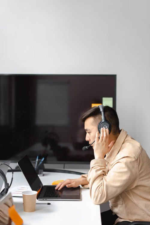 Professional in a headset taking a call at a tidy home workstation with notes and coffee nearby