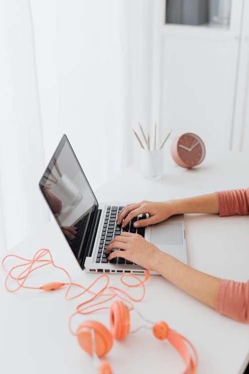 Close-up of hands typing on a laptop with a headset resting on the desk
