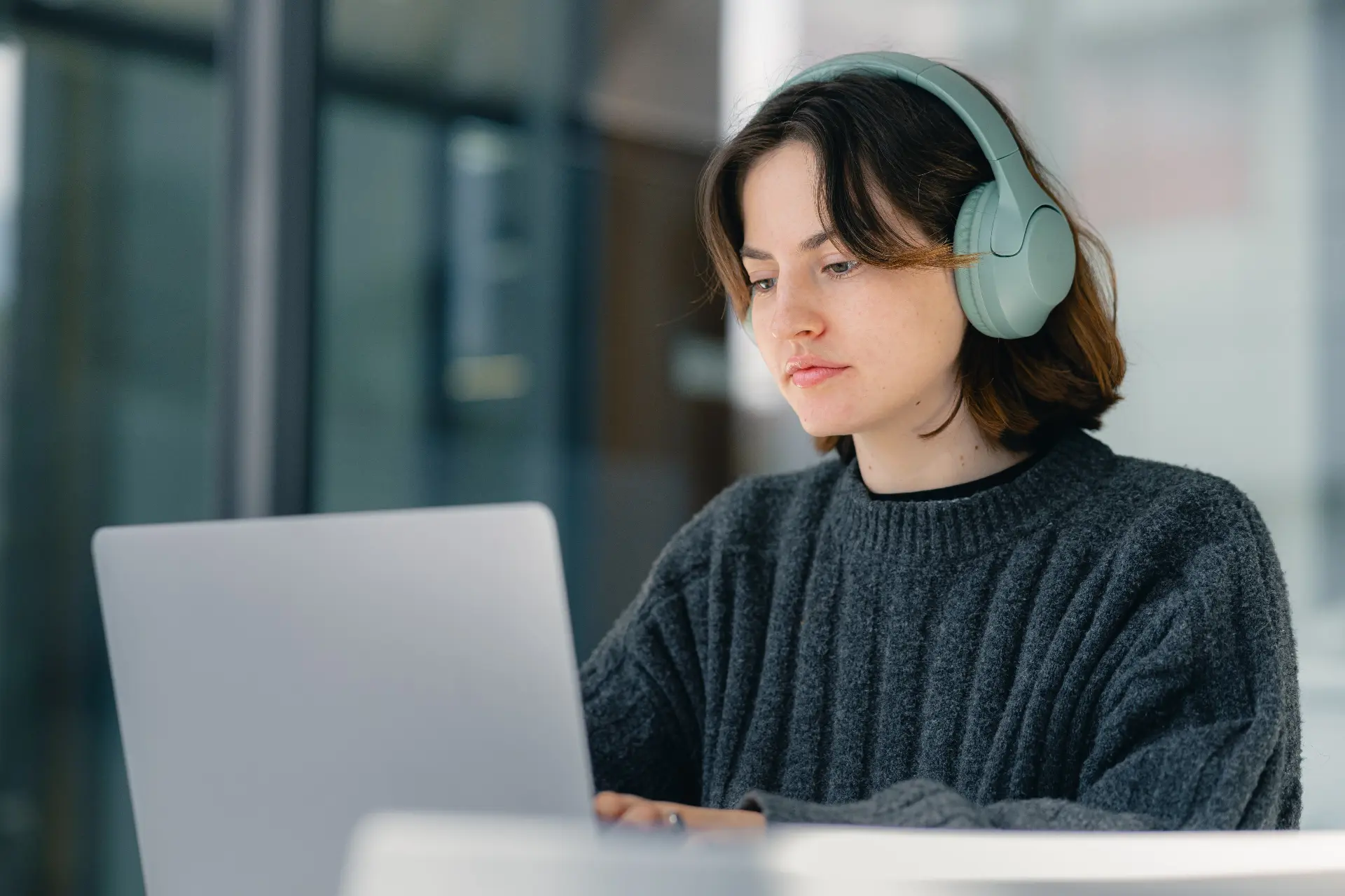 Independent customer support professional wearing headphones and working on a laptop in a calm, light-filled space