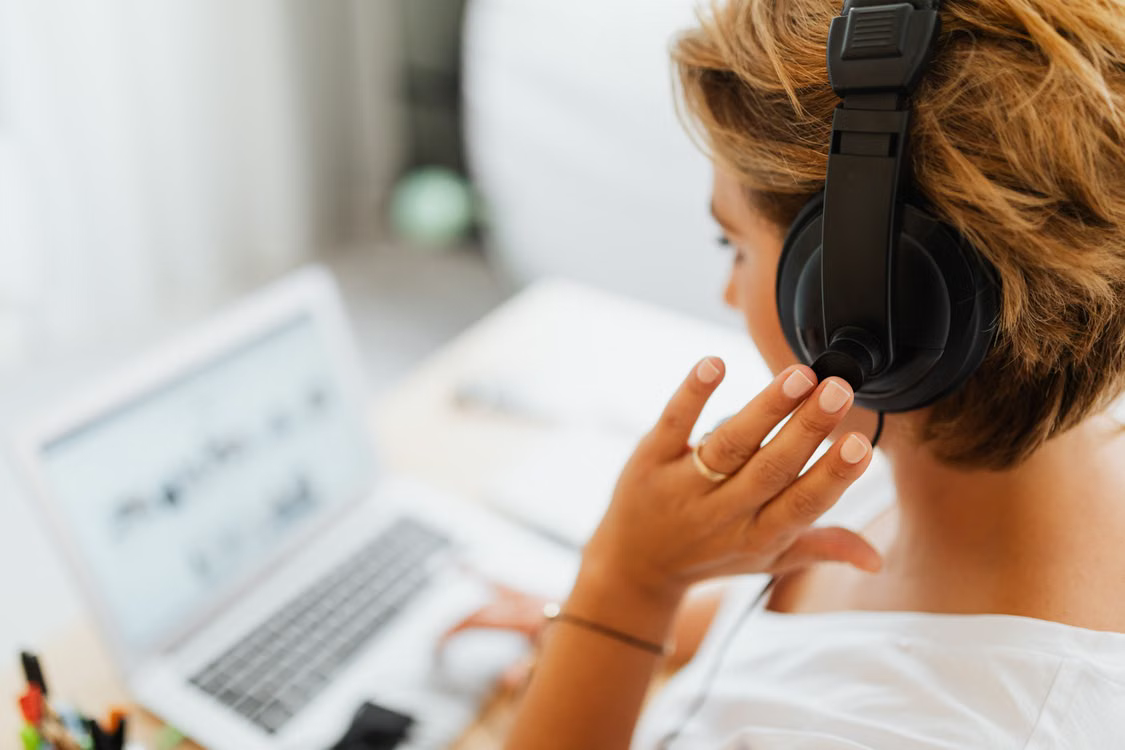 Over-the-shoulder view of a support professional adjusting a headset while working on a laptop